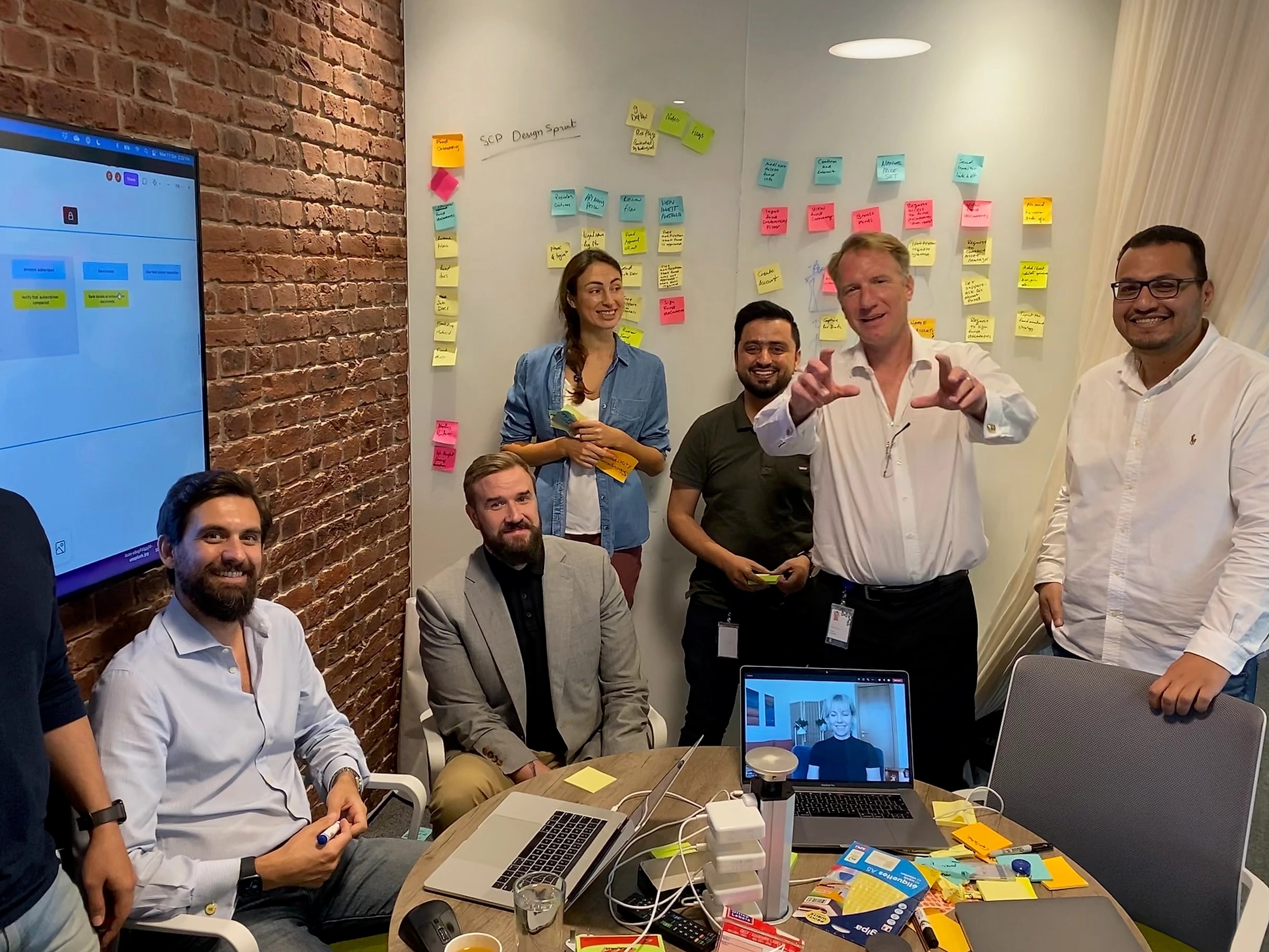 Romina with her product team at a design sprint, a sticky-note wall behind them